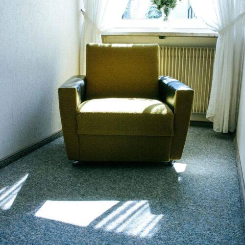 Minimalist interior featuring a cozy armchair and flower vase by a sunlit window.